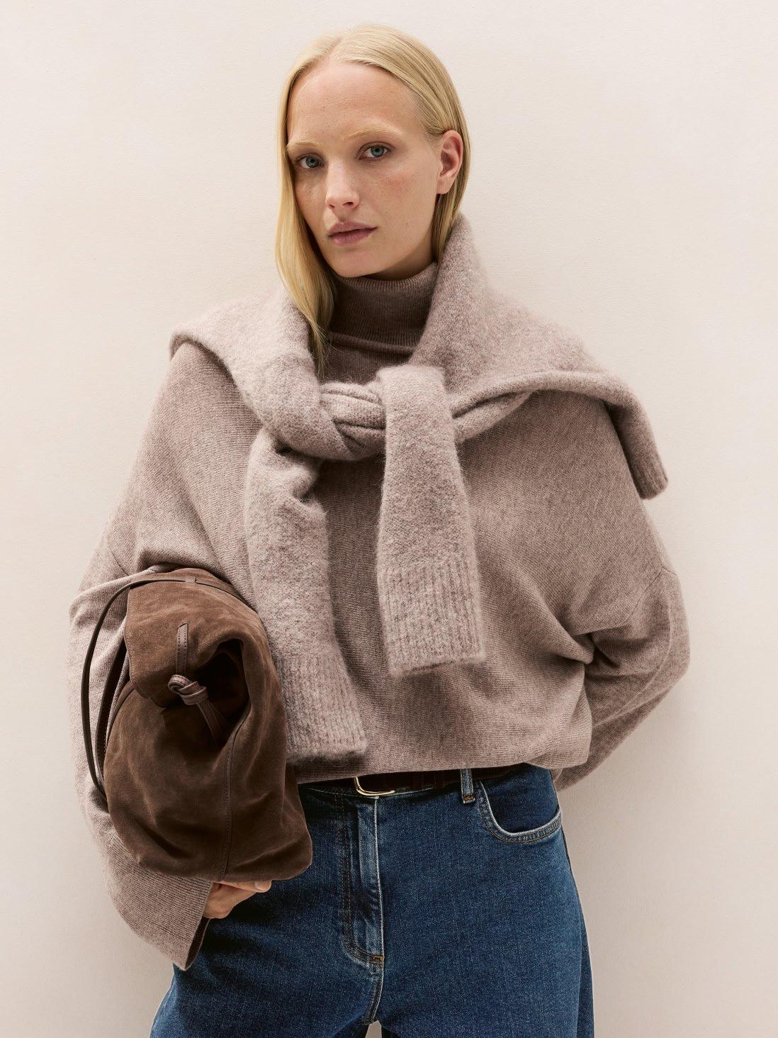 a woman in a sweater and jeans holding a purse