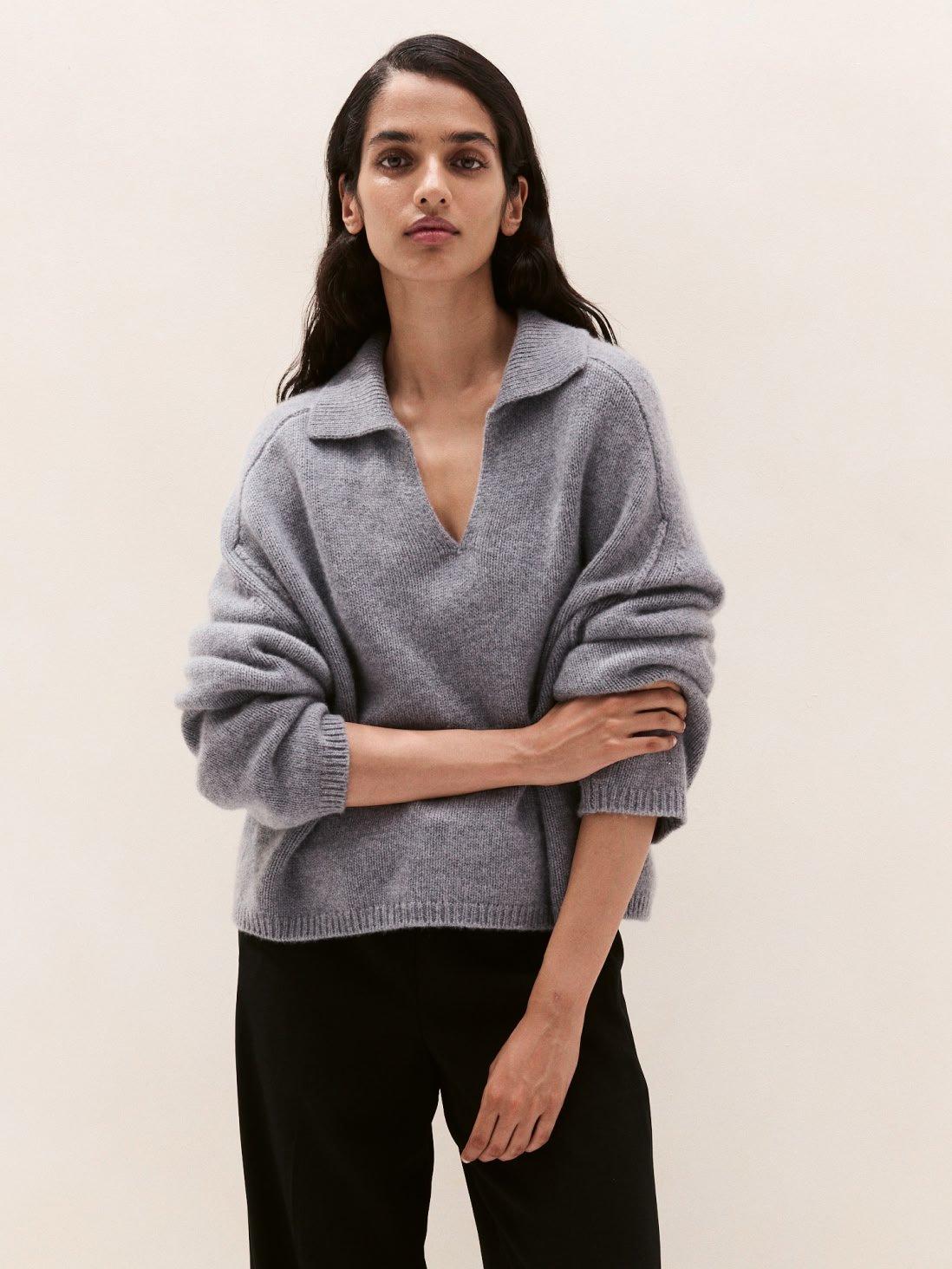 a woman in a grey sweater and black pants standing