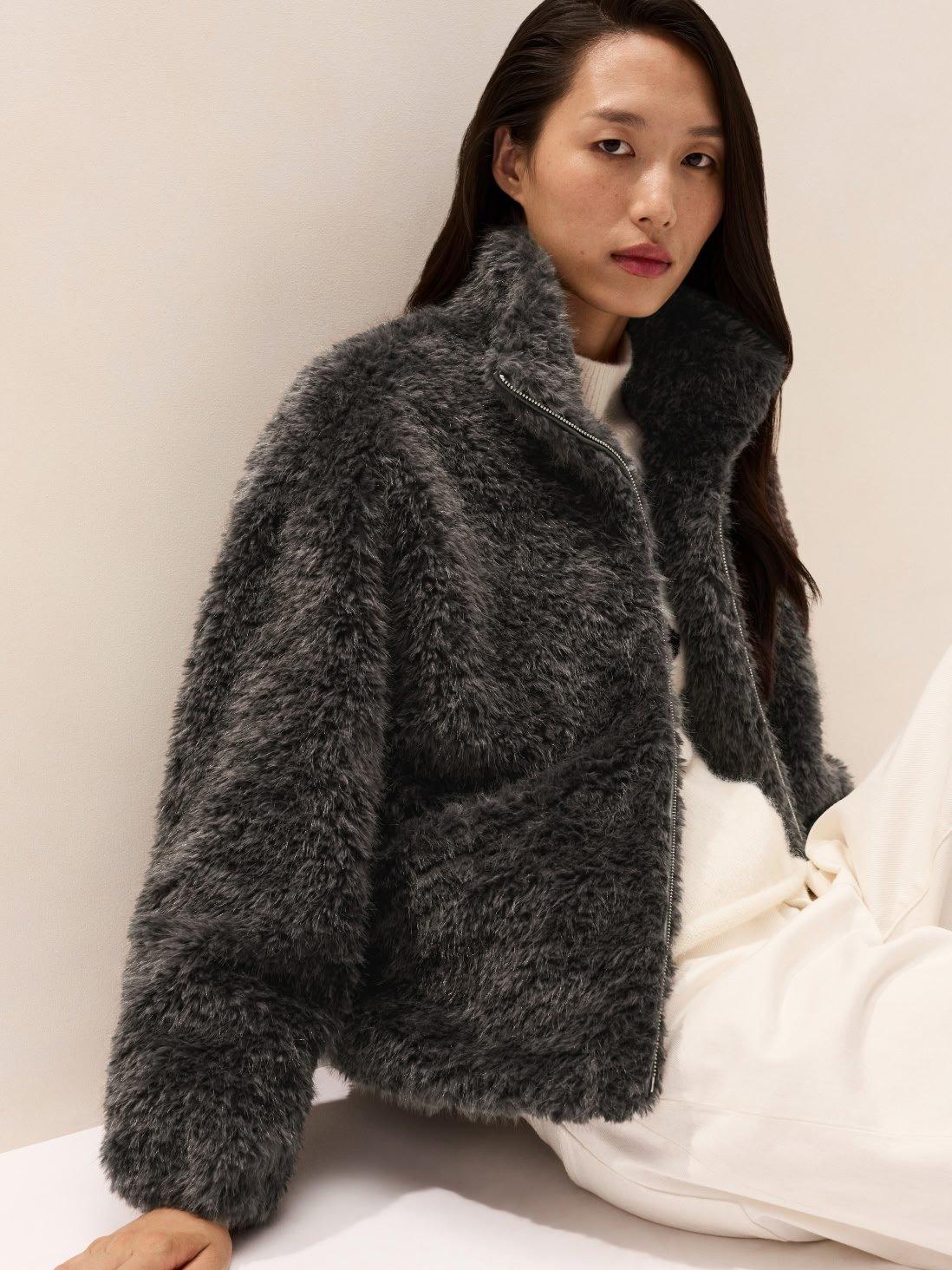 a woman in a furry jacket sitting on the floor