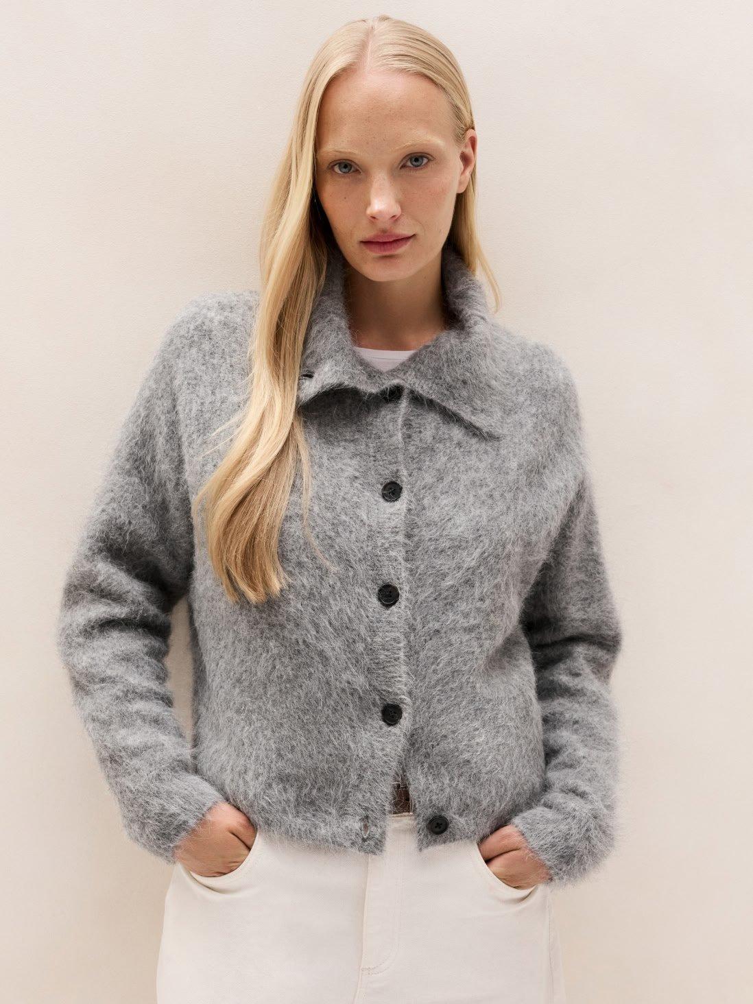 a woman in a gray sweater and white pants posing for a picture