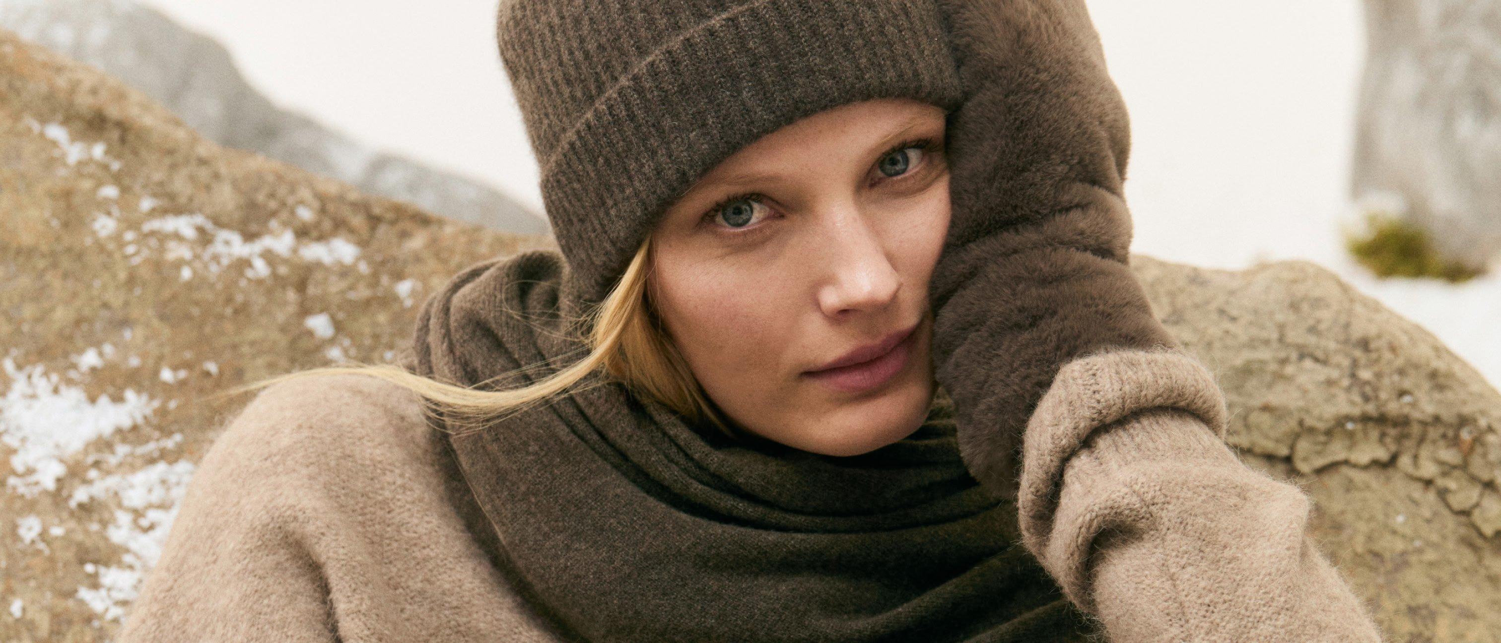 a woman in a hat and scarf sitting on a rock