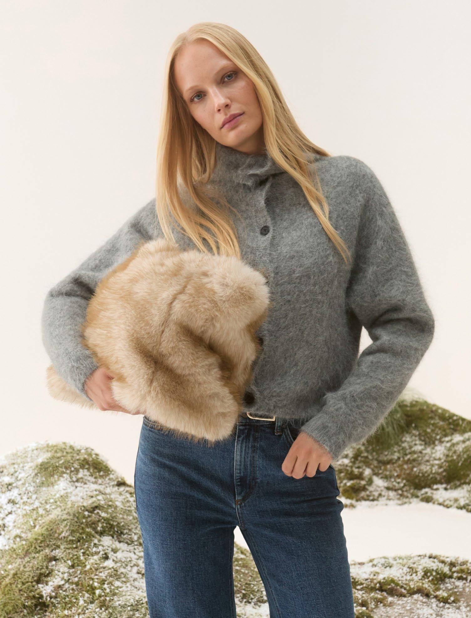 a woman in a grey sweater and jeans holding a fur coat