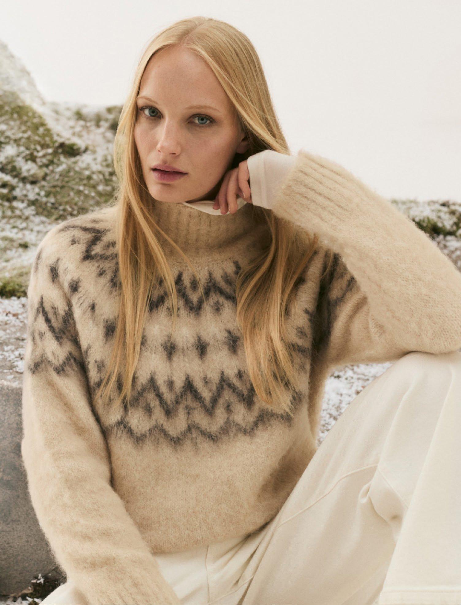 a woman in a sweater and pants sitting on a rock
