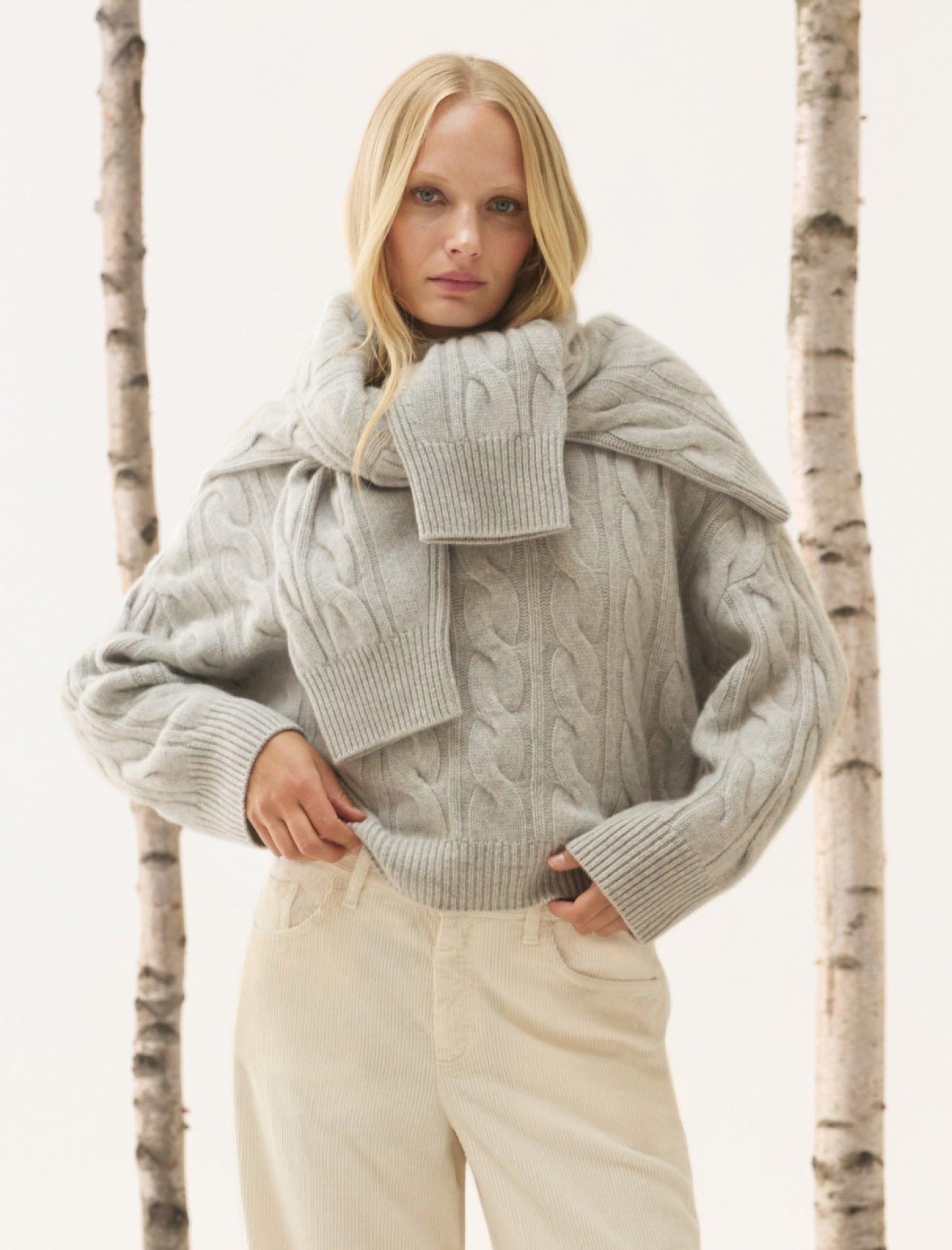 a woman in a grey sweater and white pants posing for a picture