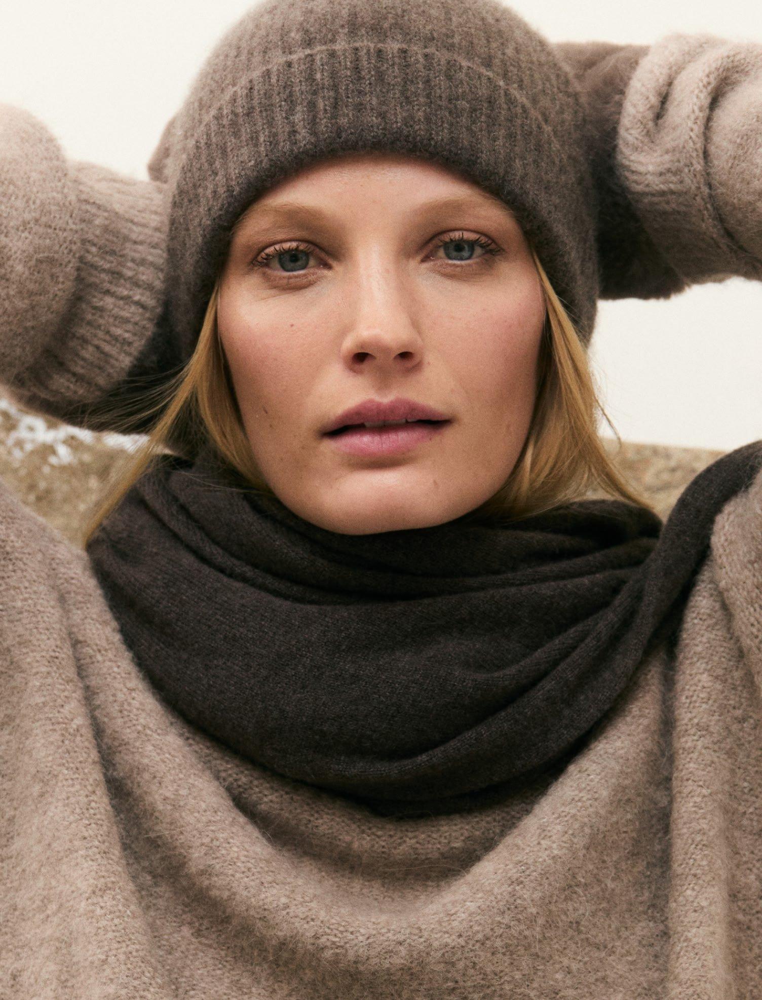 a woman in a hat and sweater holding her head