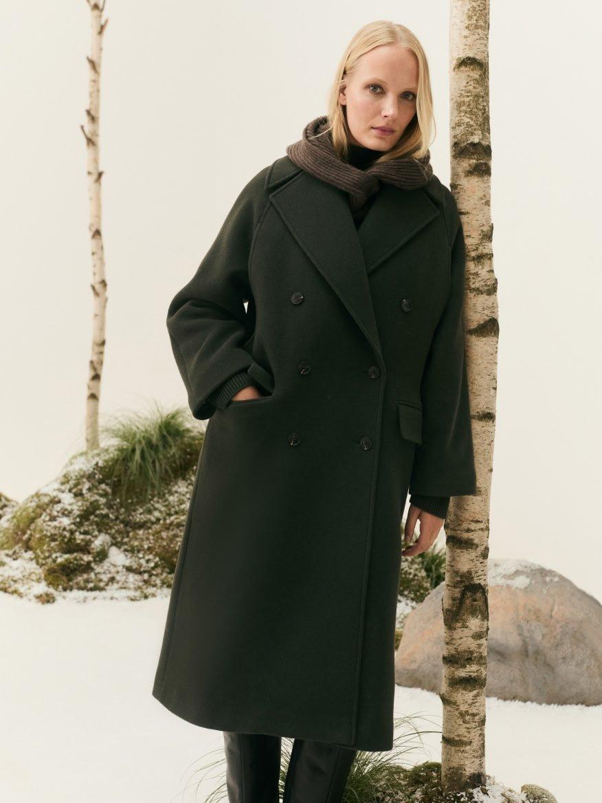 a woman in a coat standing next to a tree