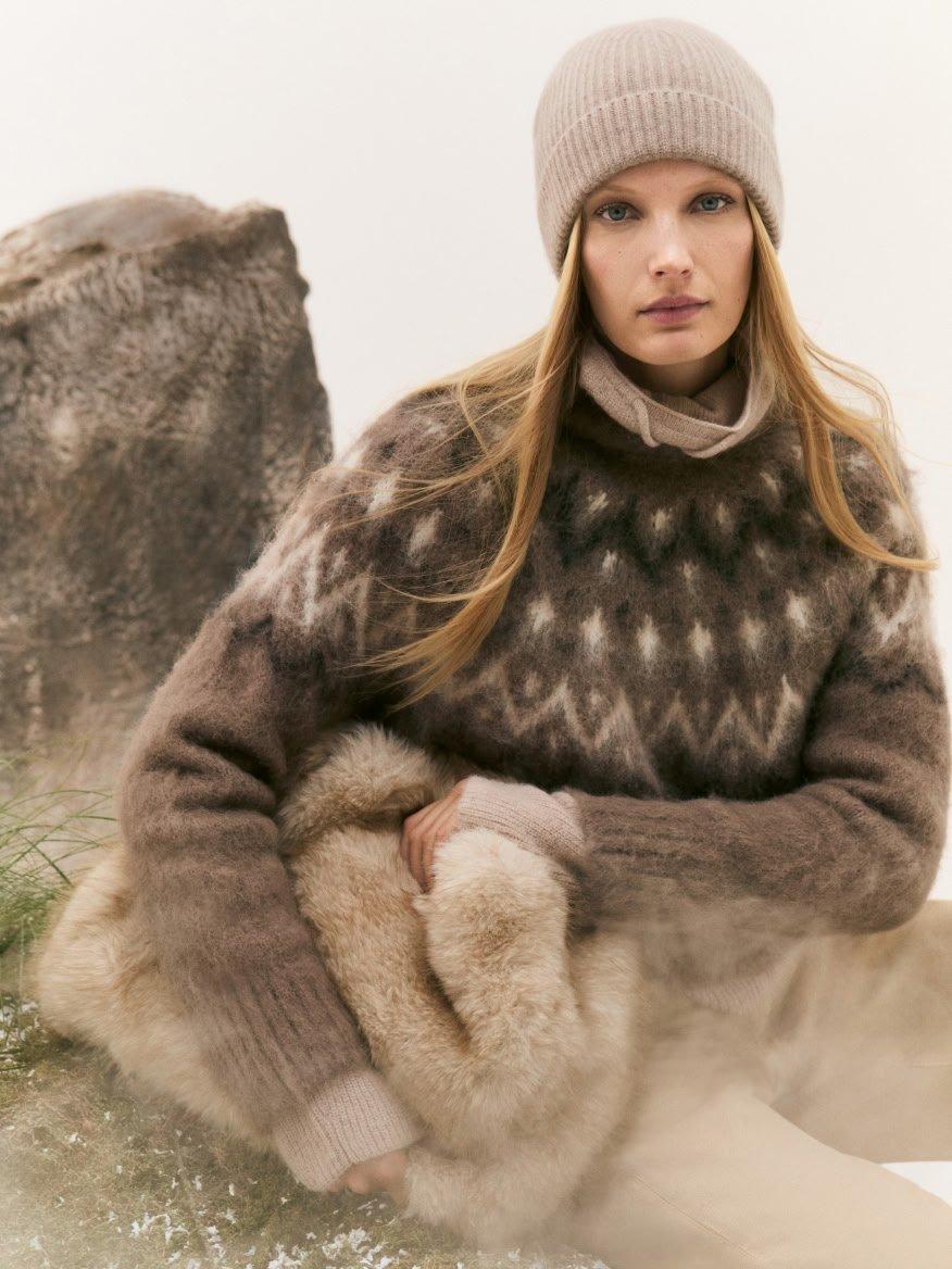 a woman in a sweater and hat sitting on a rock