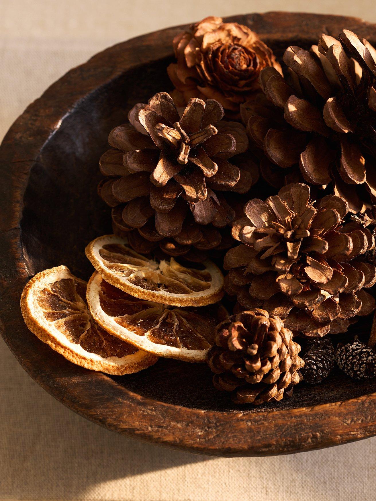 a bowl filled with pine cones, oranges and lemons