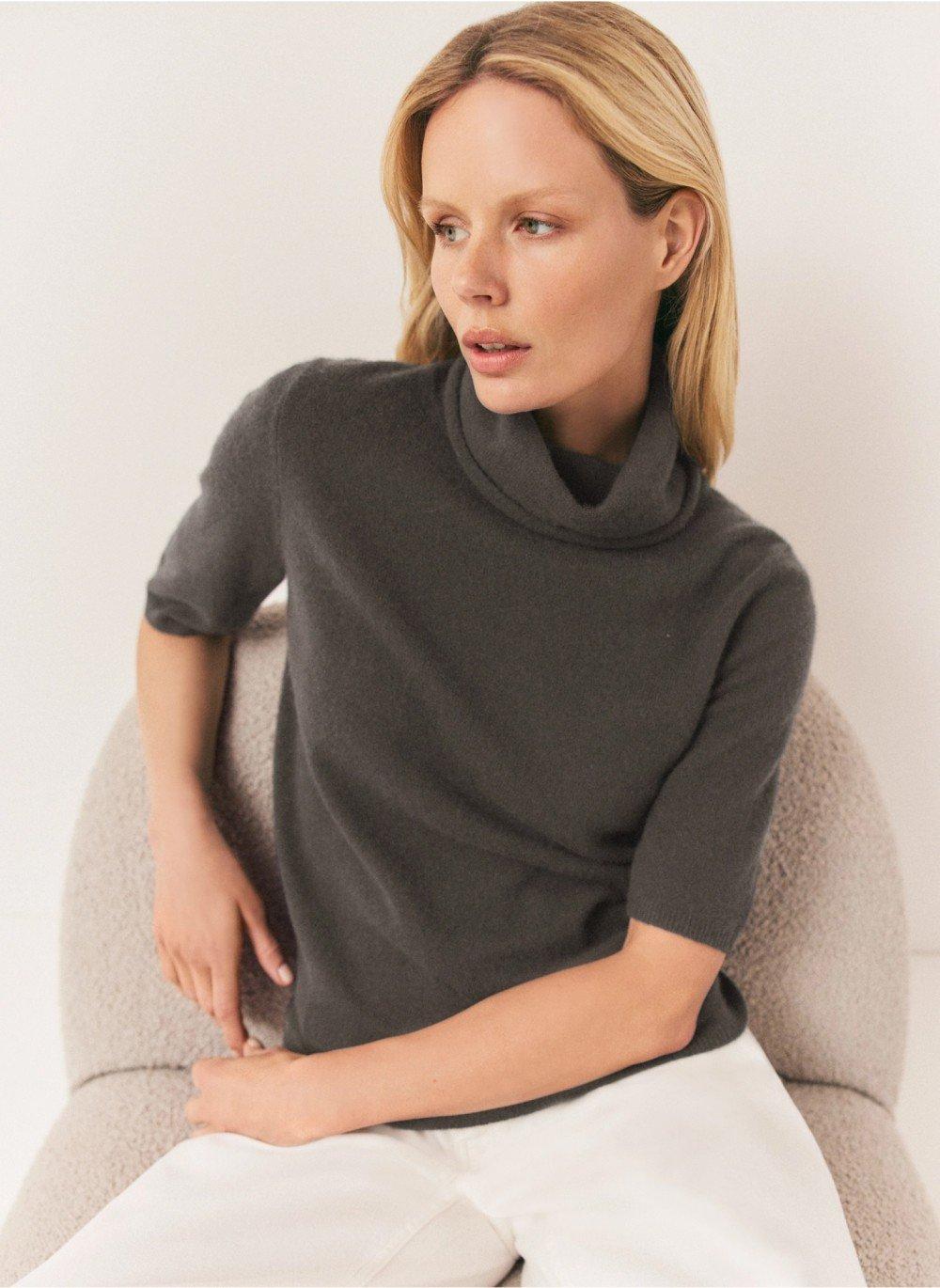 a woman sitting on a chair wearing a grey turtleneck sweater