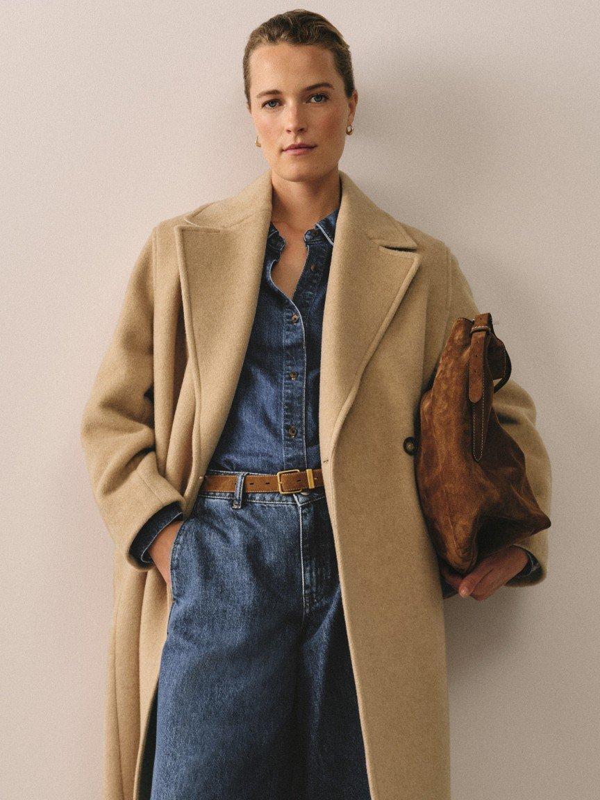a woman in a long coat and jeans holding a purse