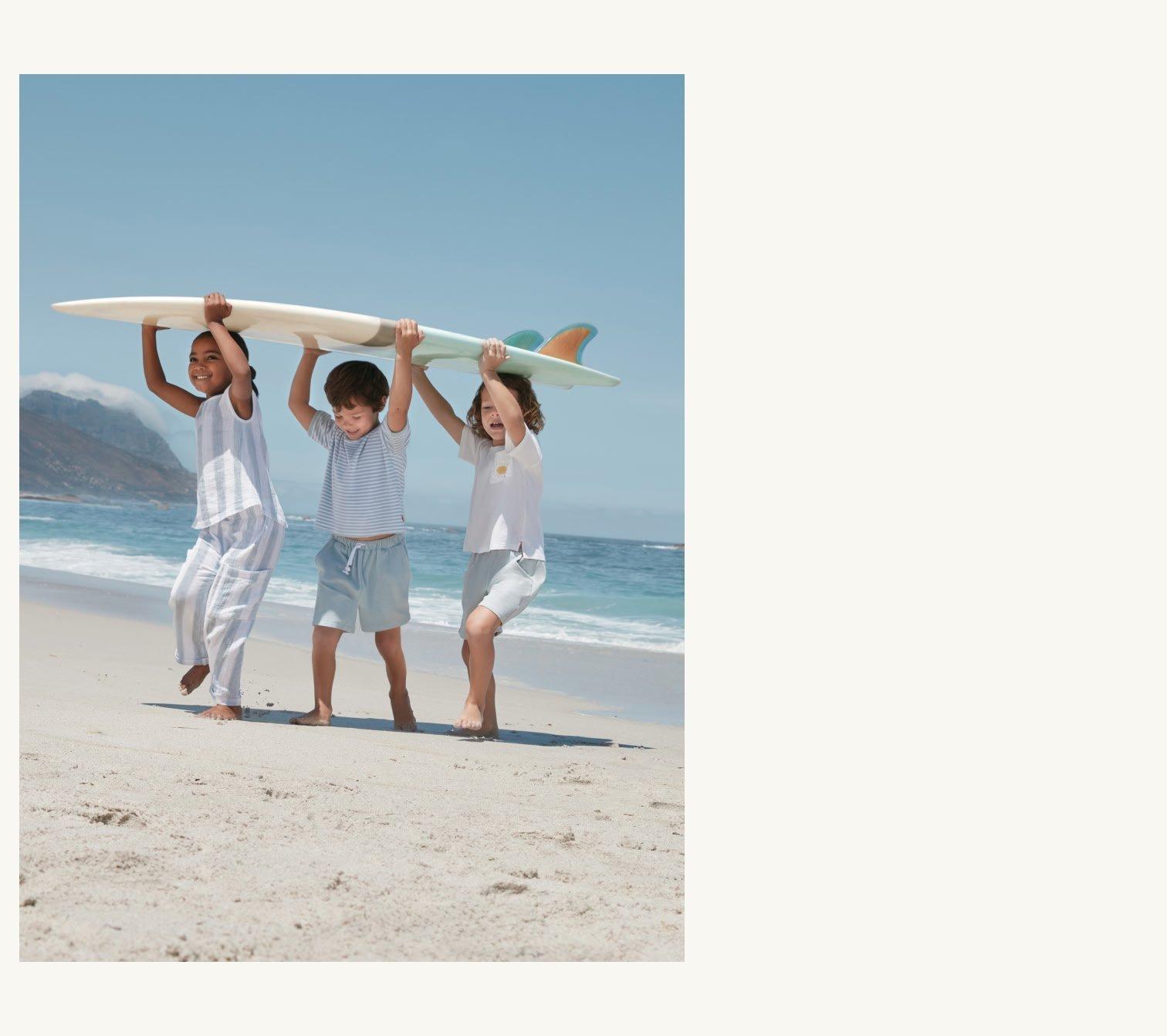 three children carrying a surfboard on the beach