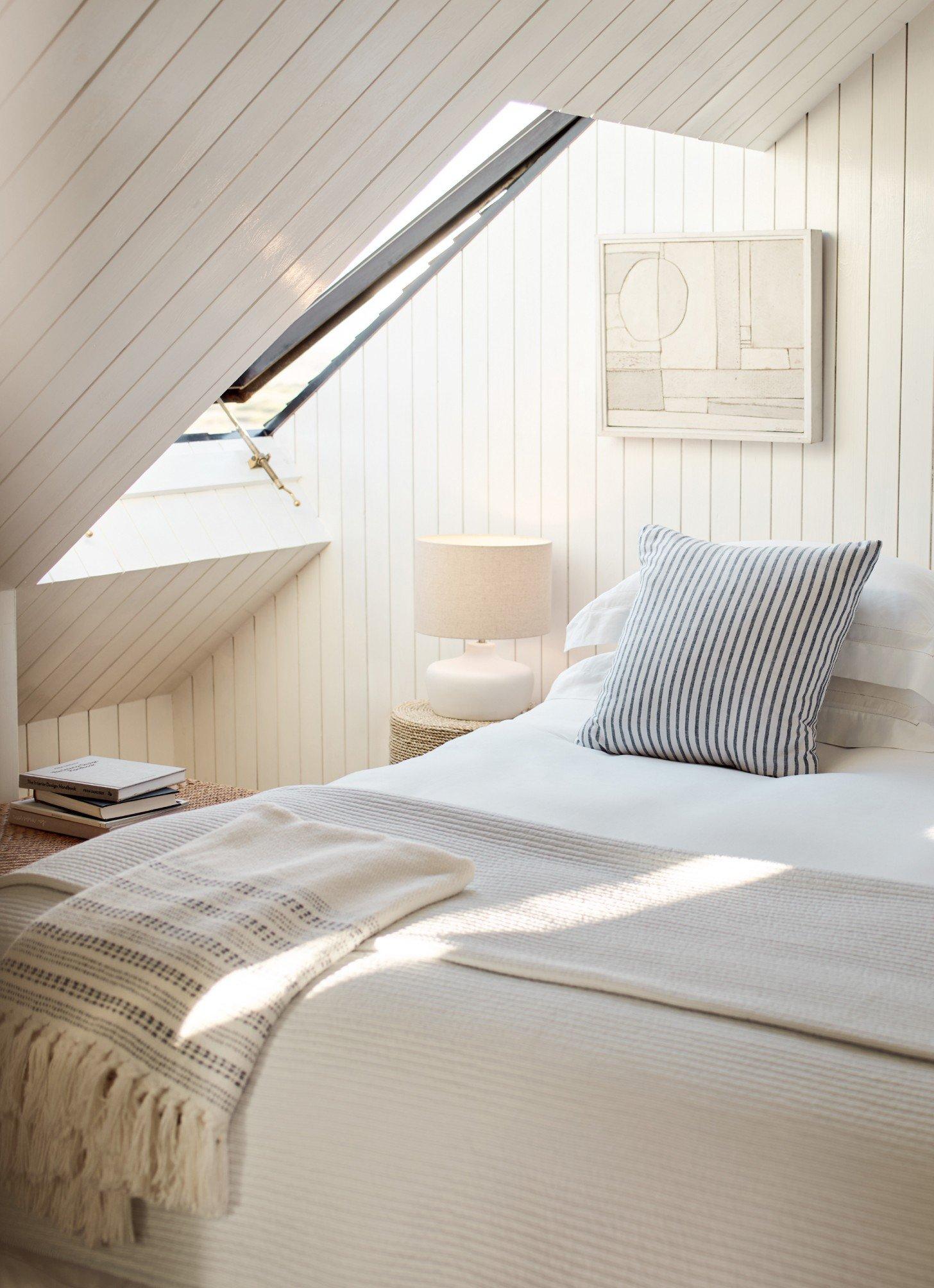 a bed with white sheets and pillows in a room with a skylight