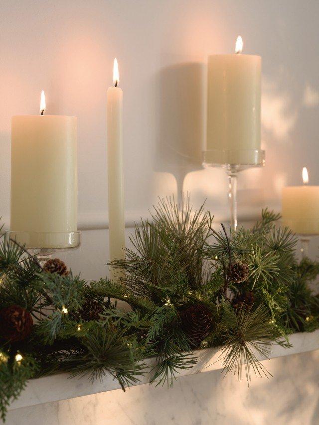 a mantle with candles and greenery with a pine tree in the background