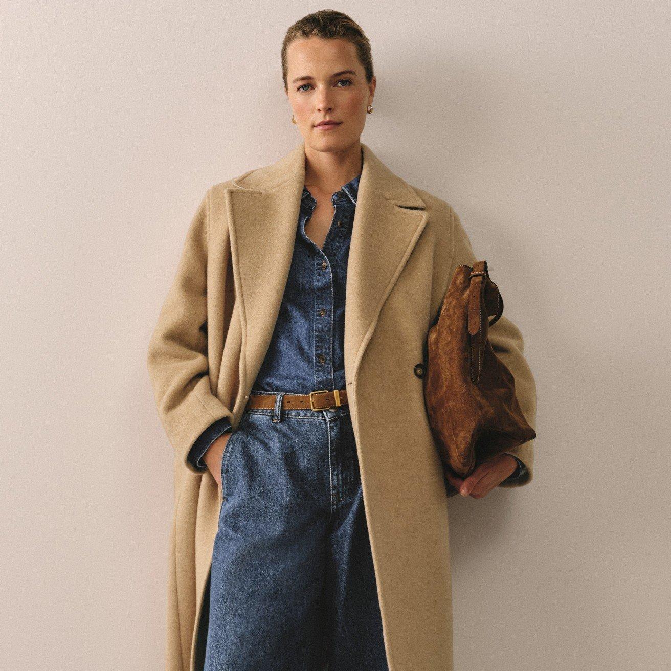 a woman in a coat and jeans holding a purse