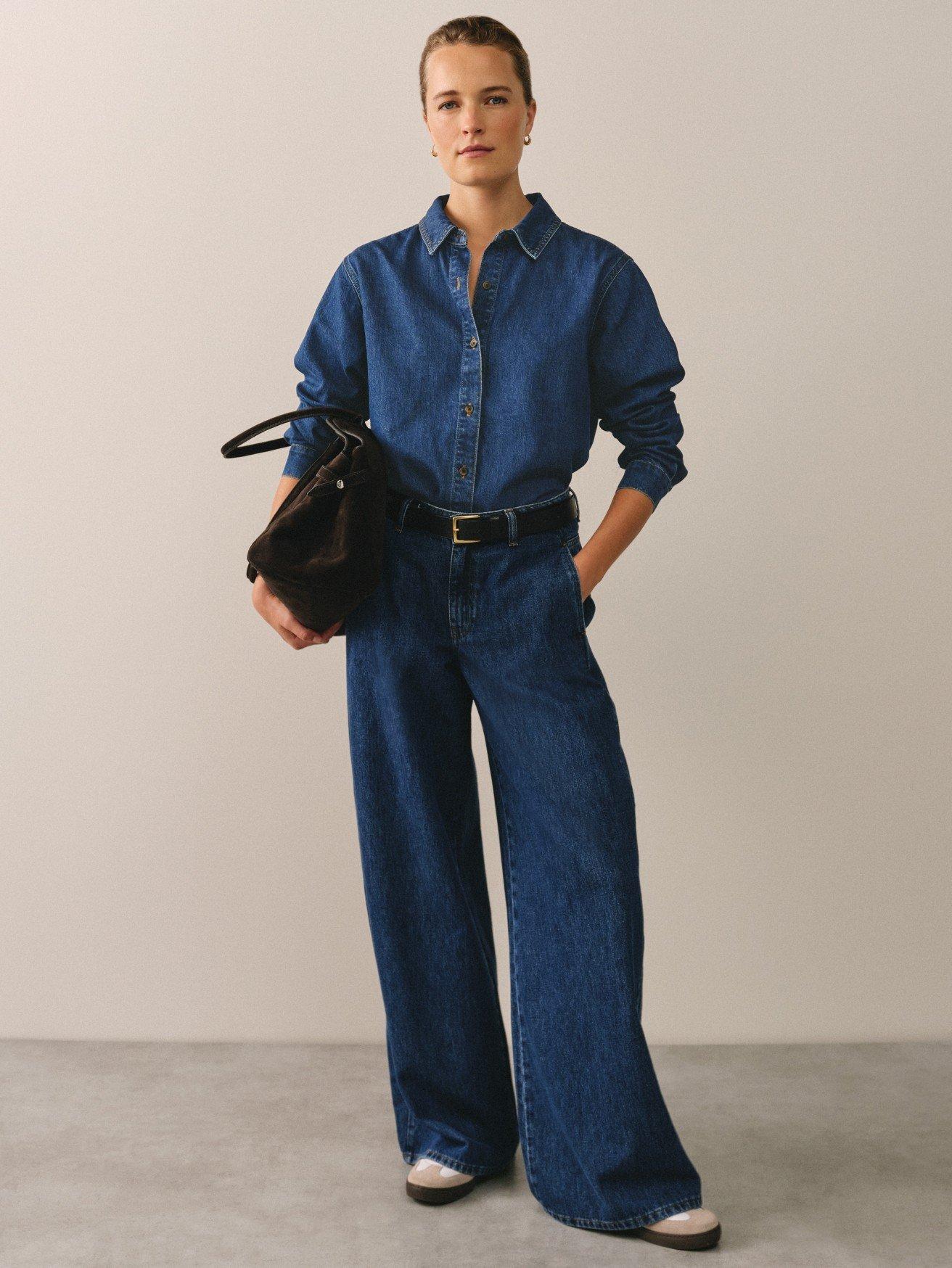 a woman in a denim jumpsuit holding a purse