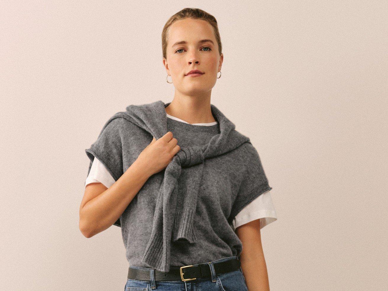 a woman in a grey sweater and jeans holding a scarf