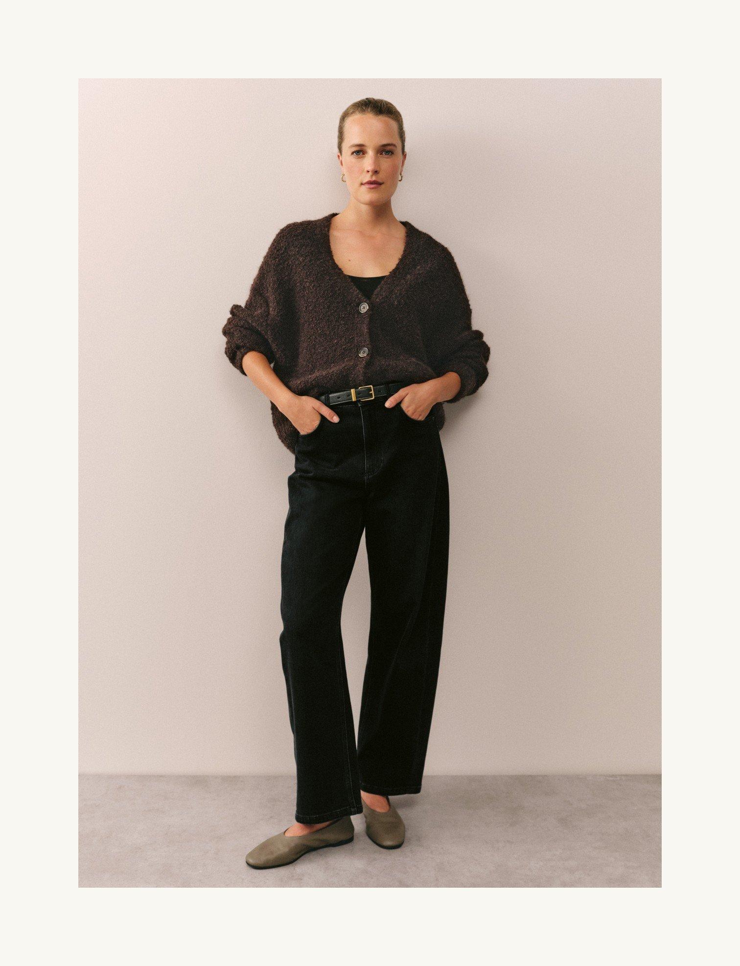 a woman in a sweater and pants standing against a wall