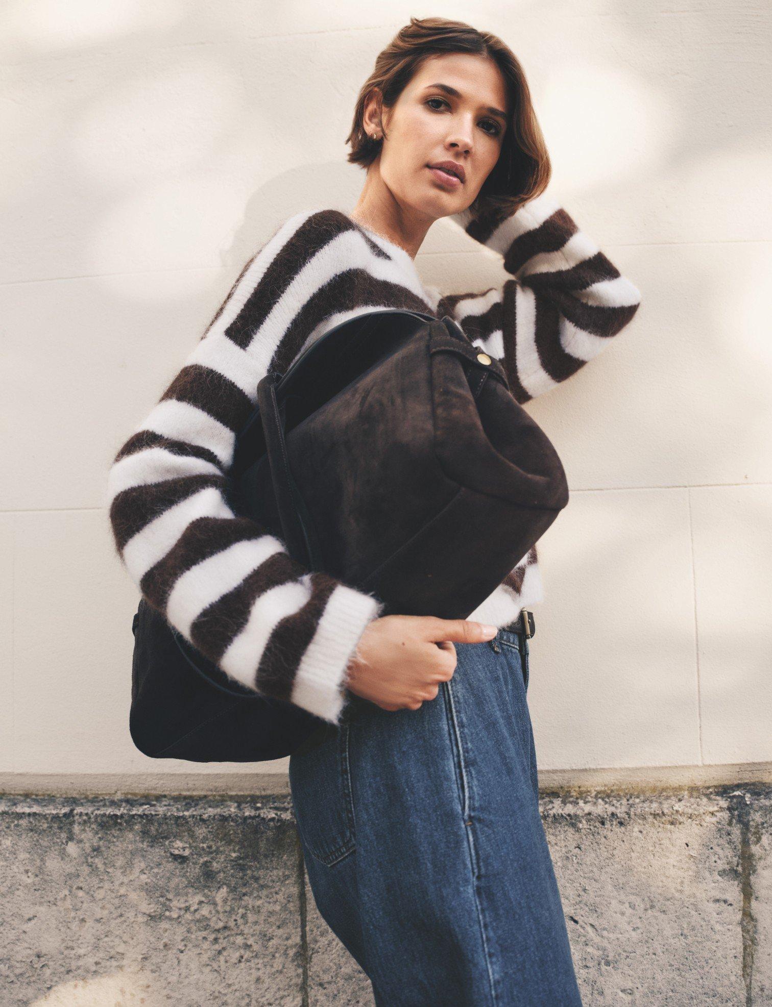 a woman in striped sweater and jeans holding a bag