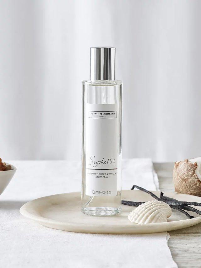 a bottle of perfume sits on a plate next to a bowl of vanilla beans