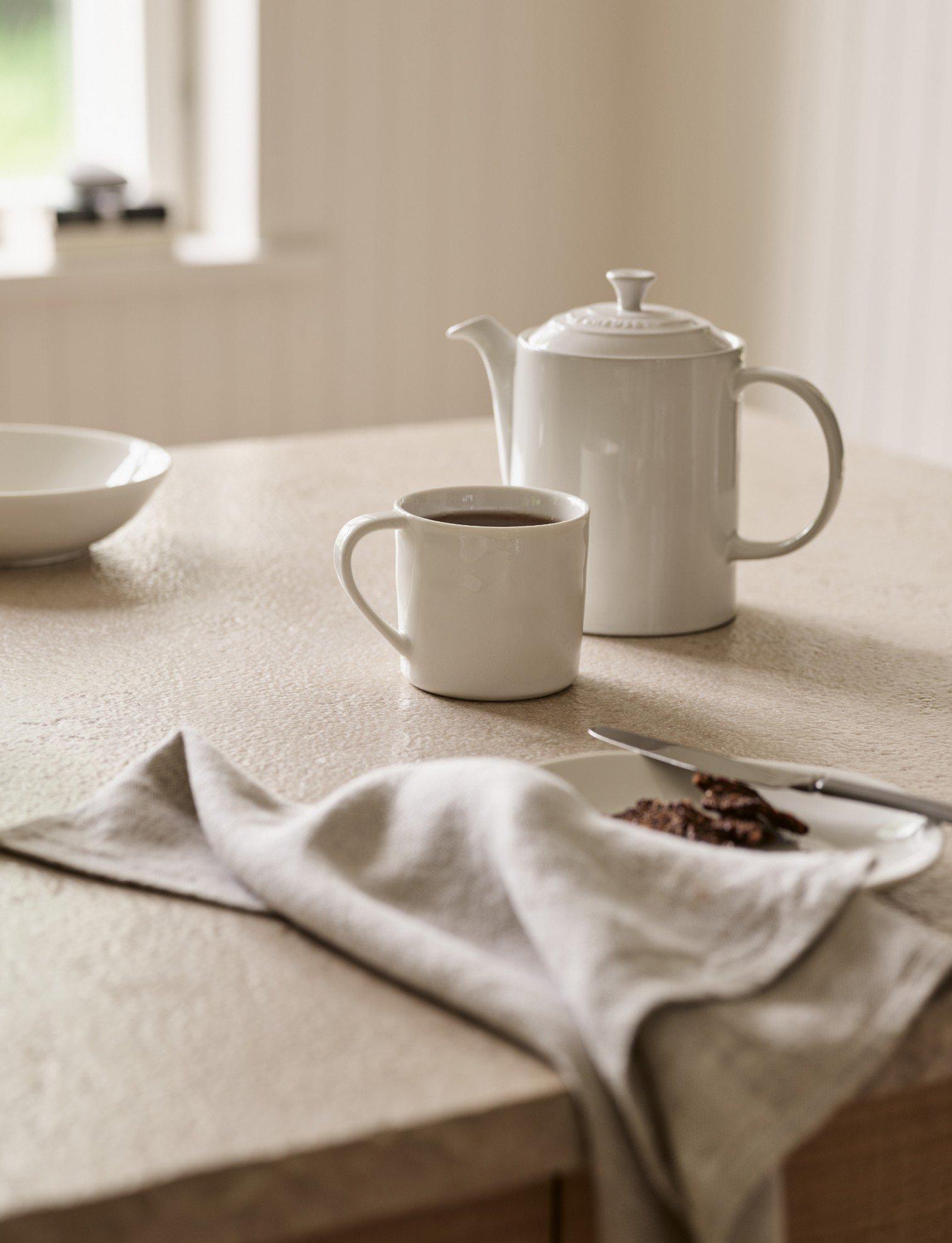 a white teapot and cup on a table with a plate of cookies