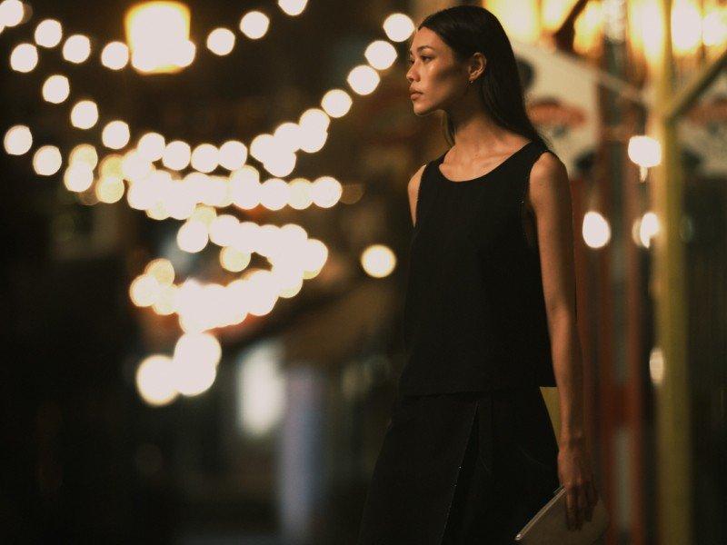 a woman standing in the middle of a street with lights in the background