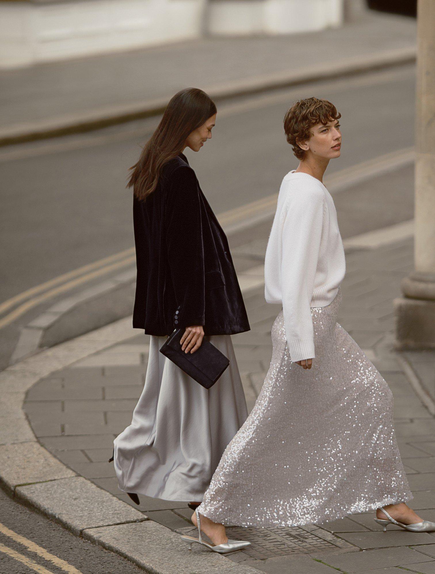 two women walking down a street in long skirts and heels