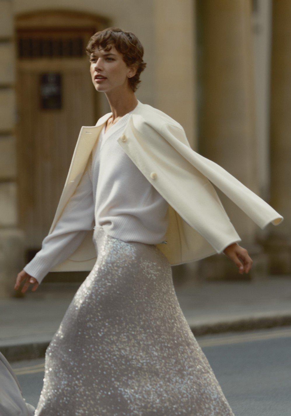 a woman in a white jacket and silver skirt walking down the street