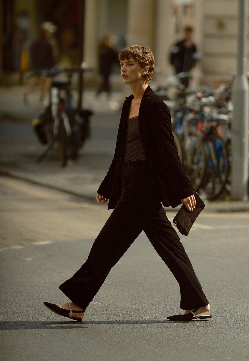 a woman in black suit walking down a street with a purse