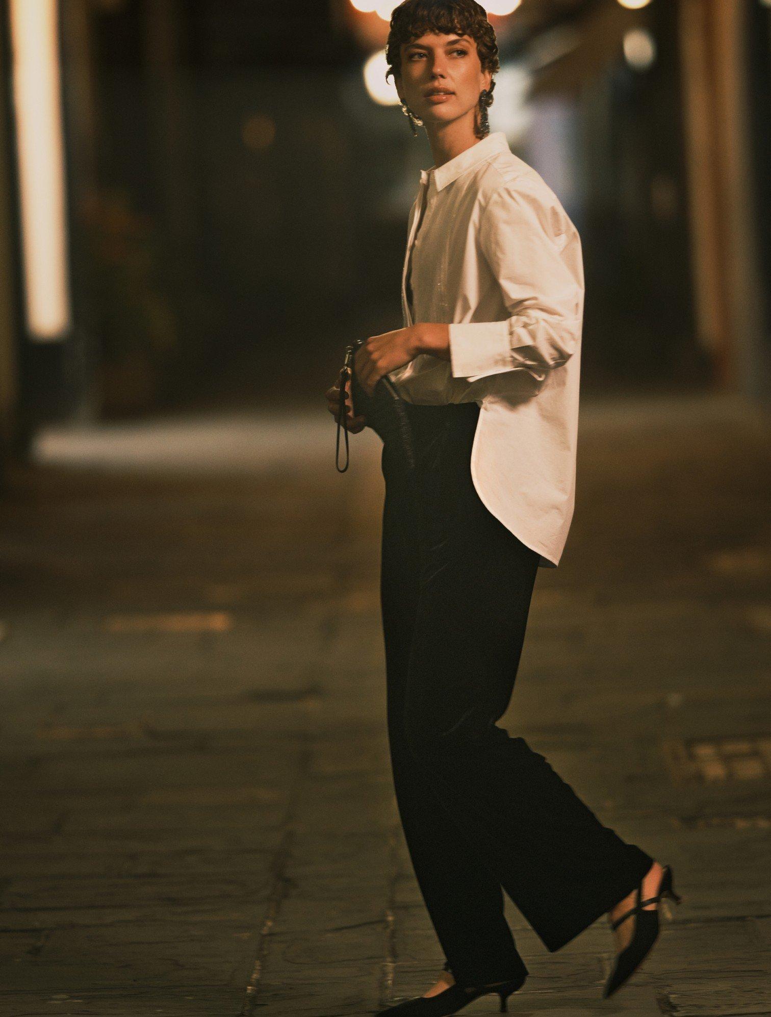 a woman walking down a street in a white shirt and black pants