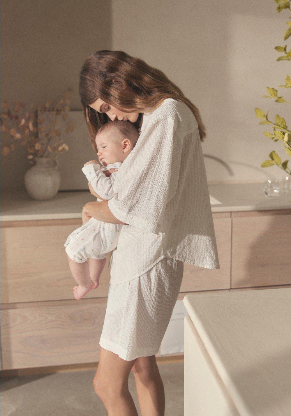 a woman in white standing in a kitchen holding a baby