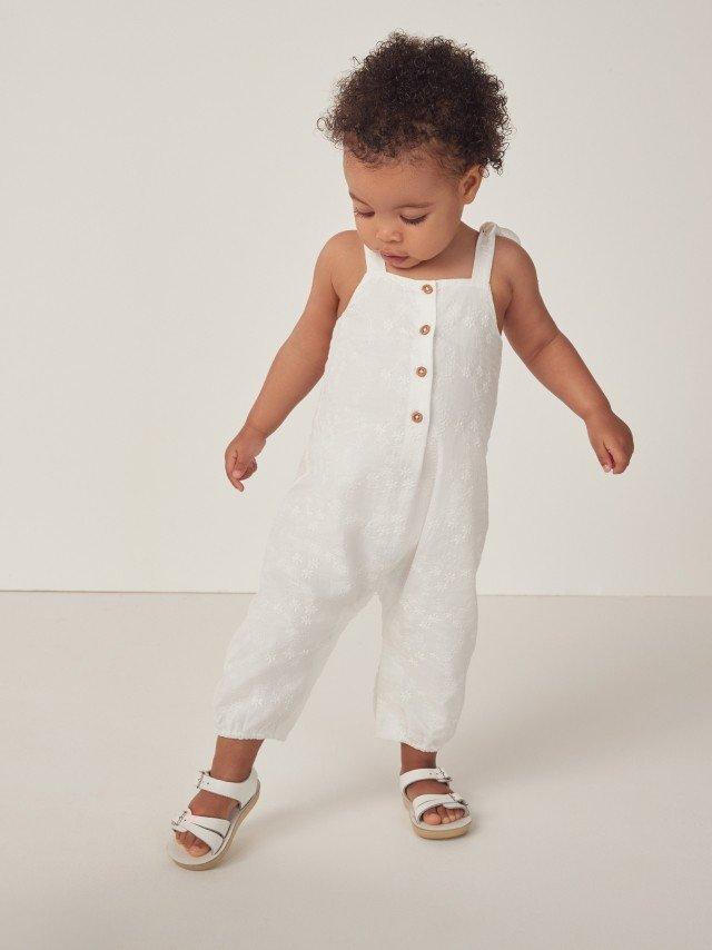 a baby girl in white overalls and sandals