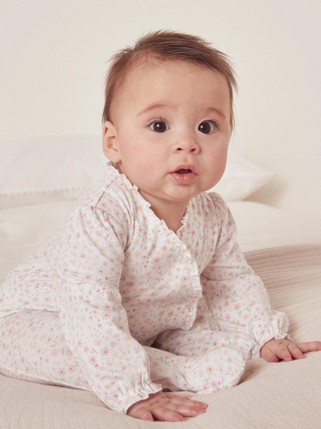 a baby sitting on a bed with a white sheet