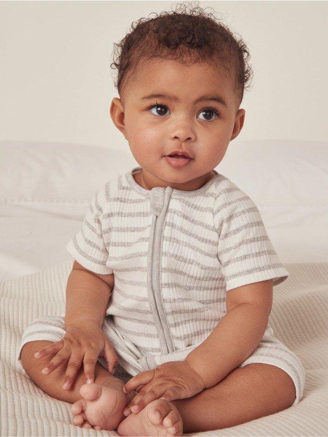 a baby sitting on a bed with a white and gray striped shirt