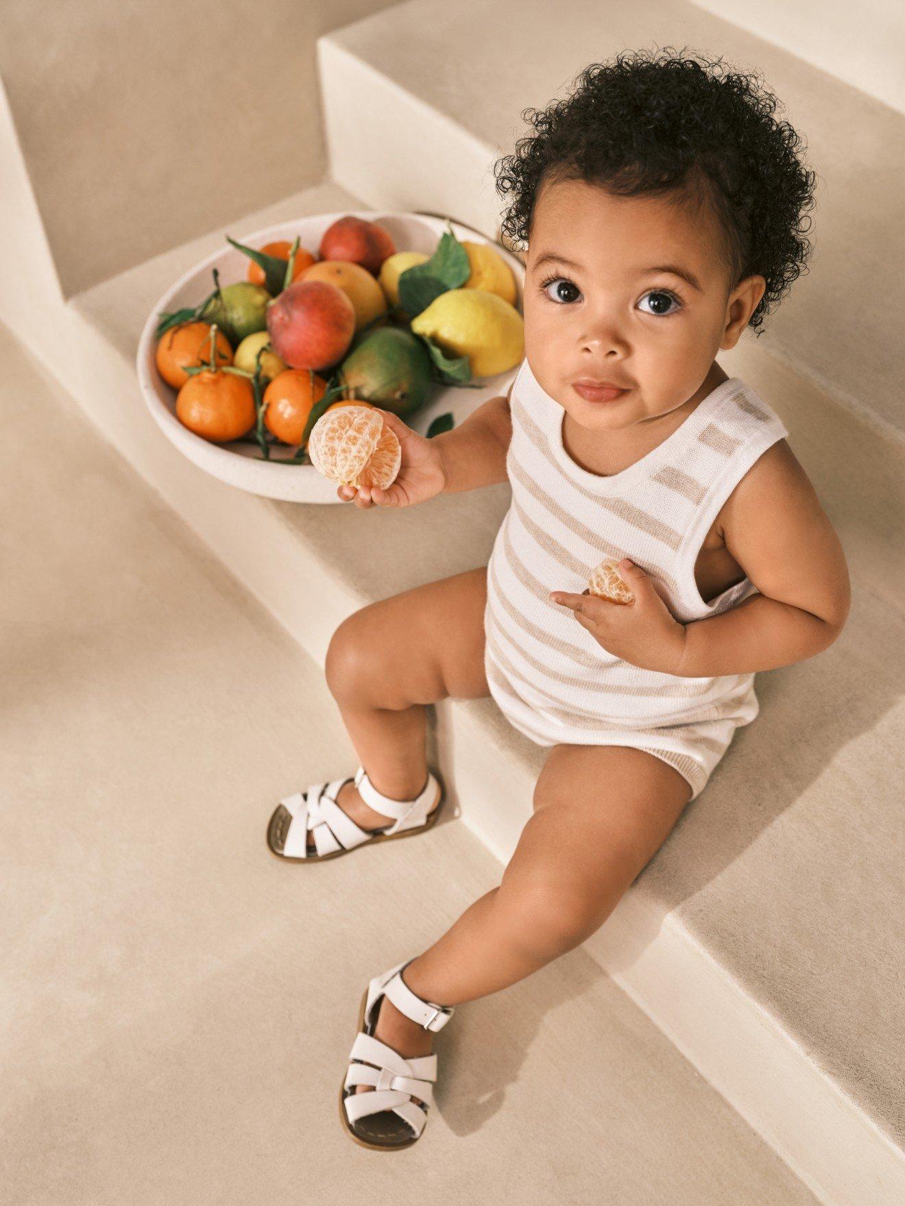 a baby sitting on steps with a bowl of fruit