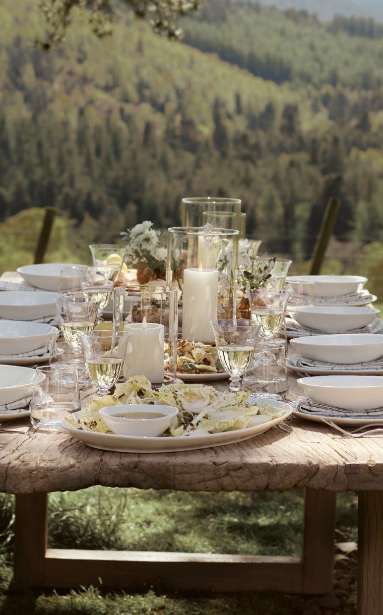 a table set with plates and glasses and candles on a hillside