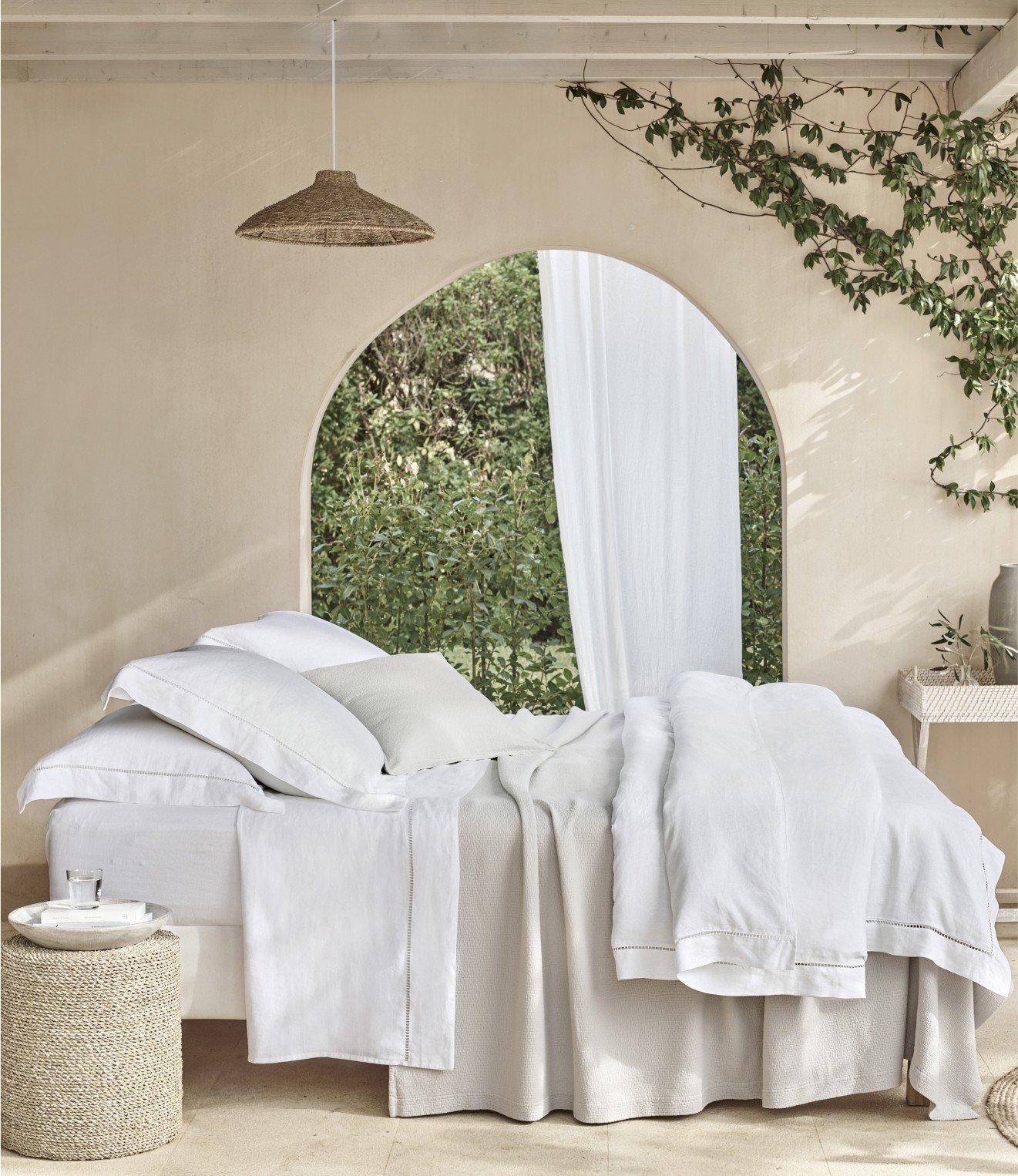 a bed with white sheets and pillows in a room with a window