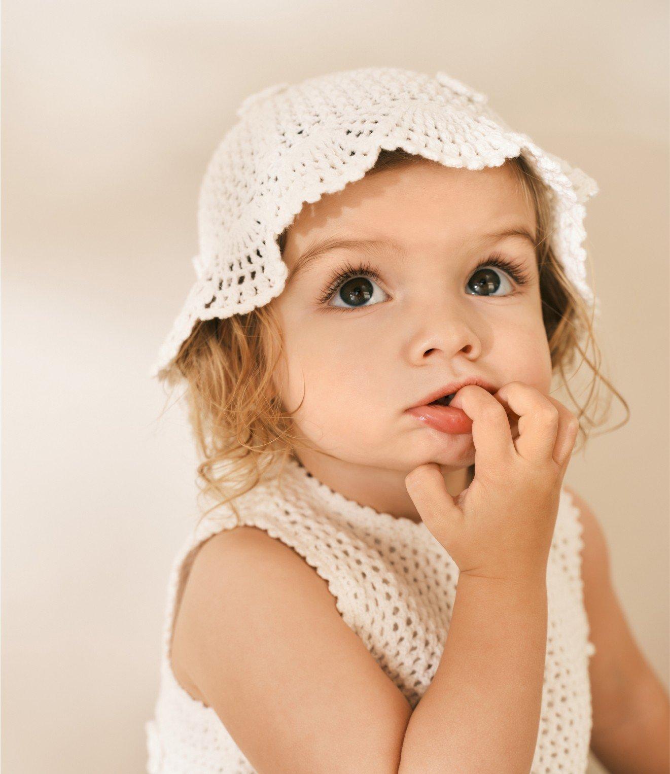 a little girl wearing a white dress and a white hat