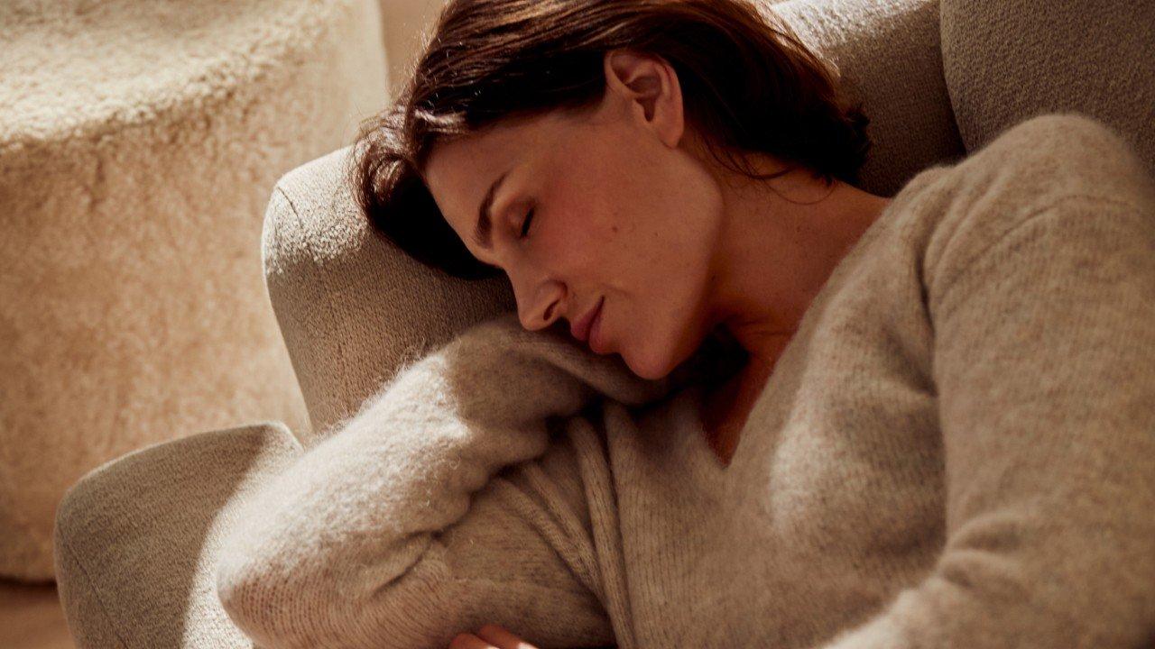 a woman in a sweater sleeping on a couch with a cat