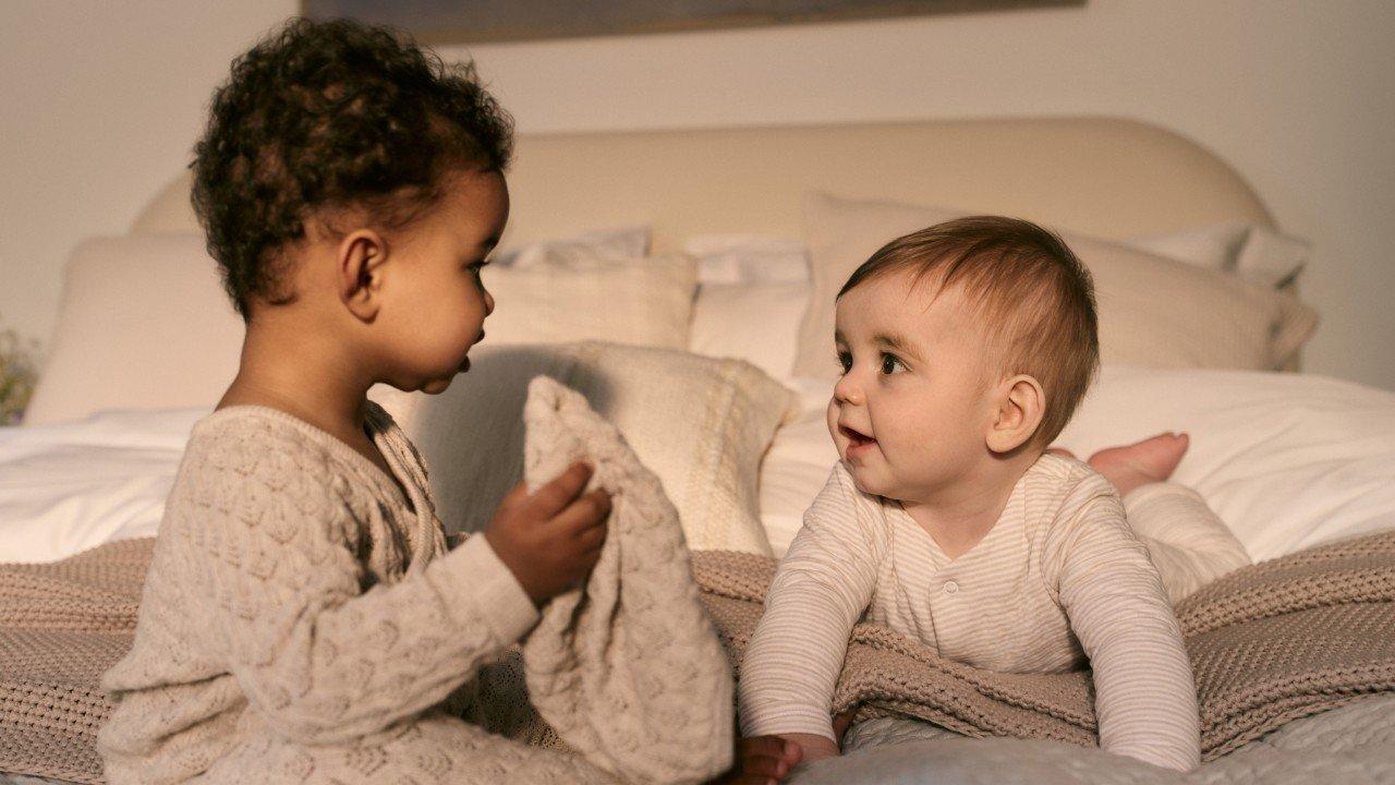 two babies playing on a bed with a blanket and a toy