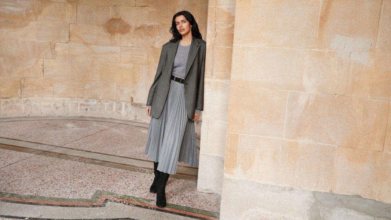 a woman in a gray dress and black boots standing in a hallway