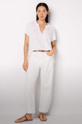 a woman in white pants and sandals standing against a white wall