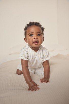 a baby in a white onesie smiling on a bed