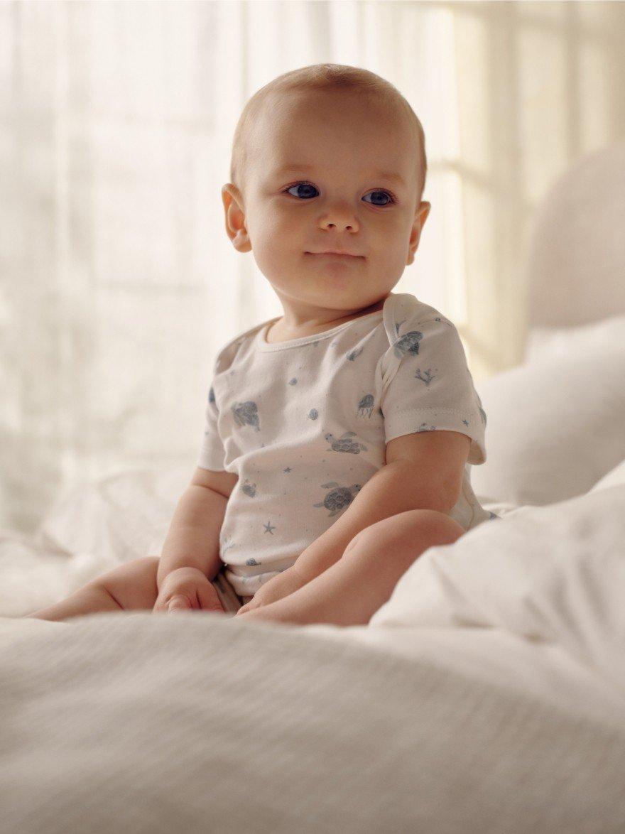 a baby sitting on the bed smiling 