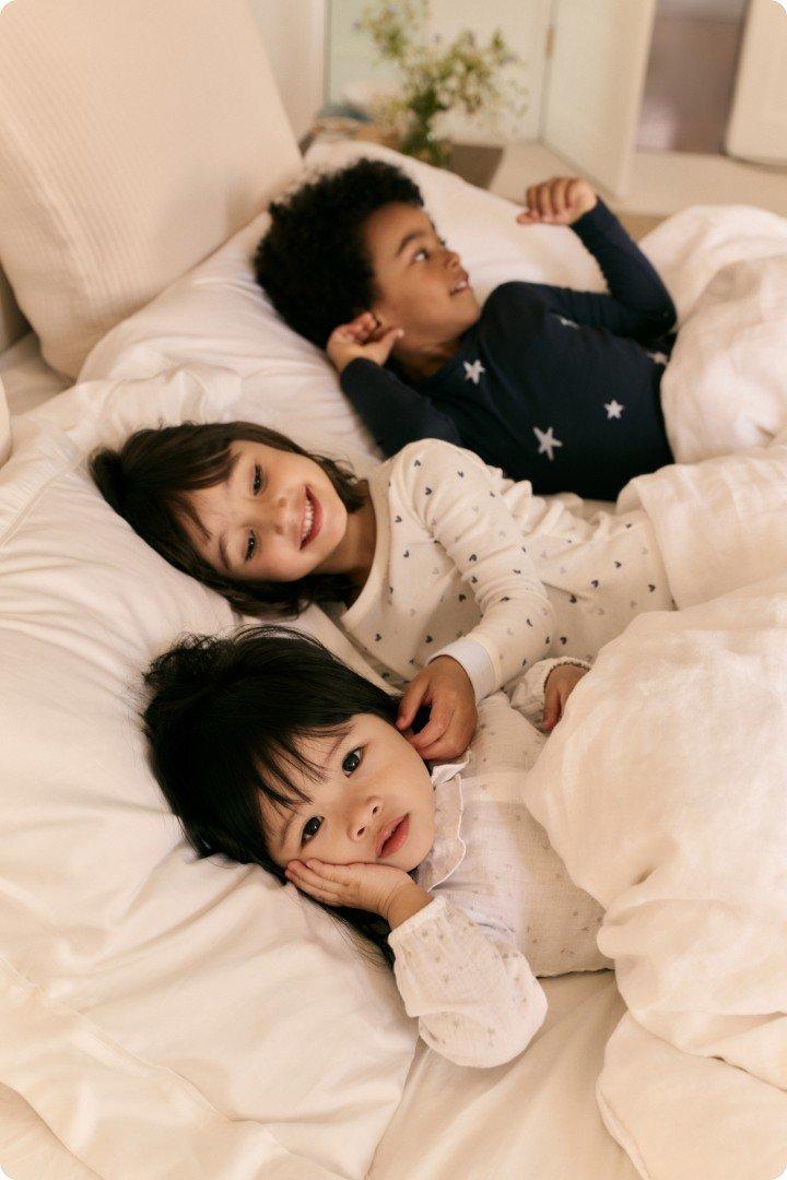 three children laying in bed together on a white bed