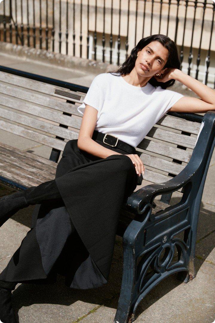 a woman sitting on a bench in a white shirt and black skirt