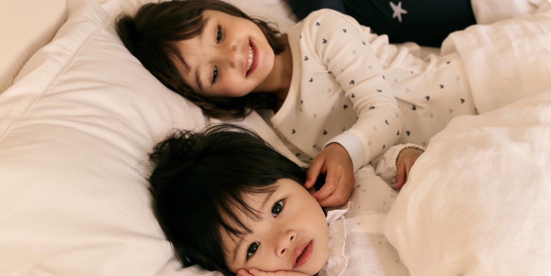 two children laying in bed together smiling at the camera