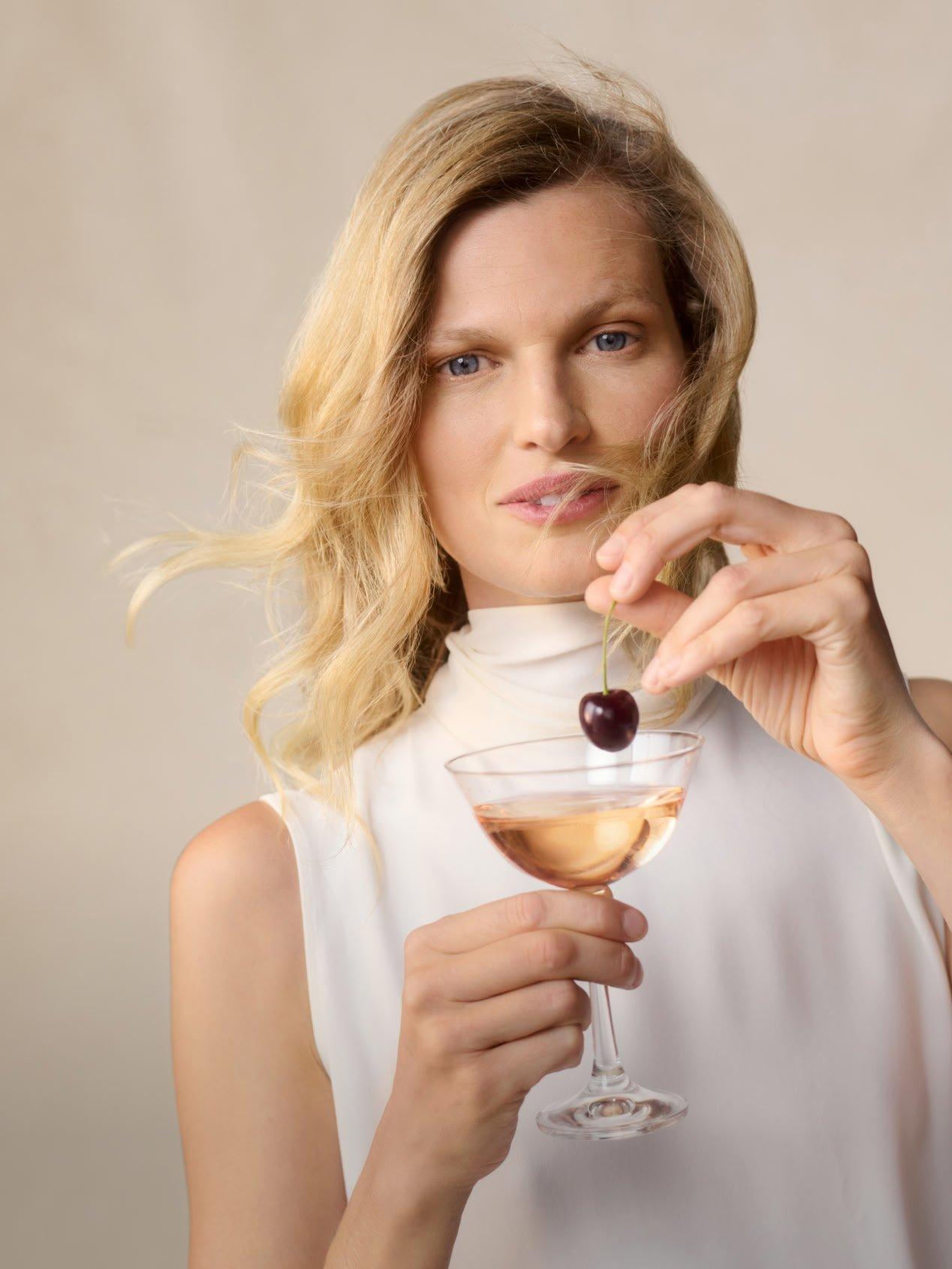 a woman holding a glass of wine with a cherry in it