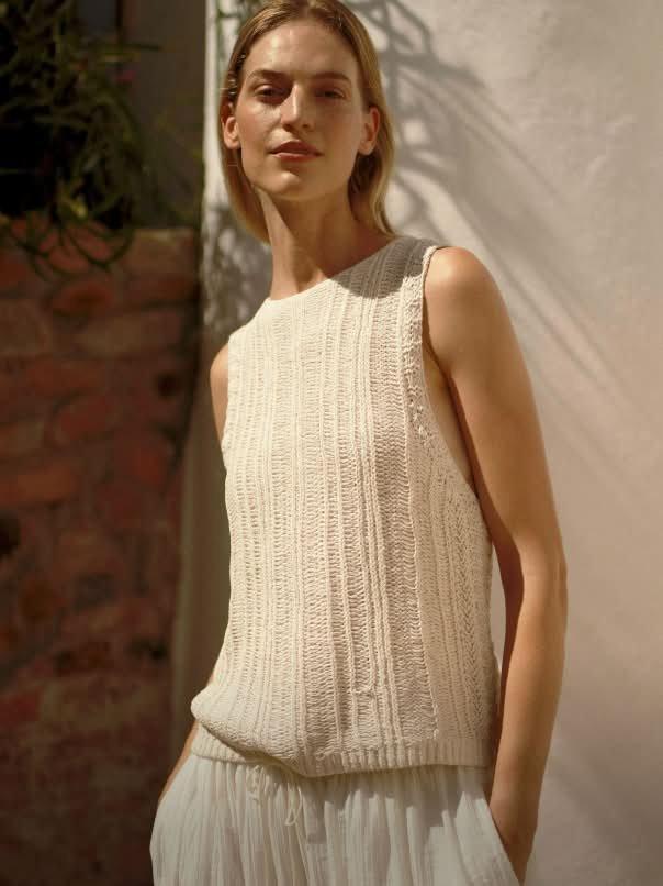 a woman in a white top and pants standing next to a wall