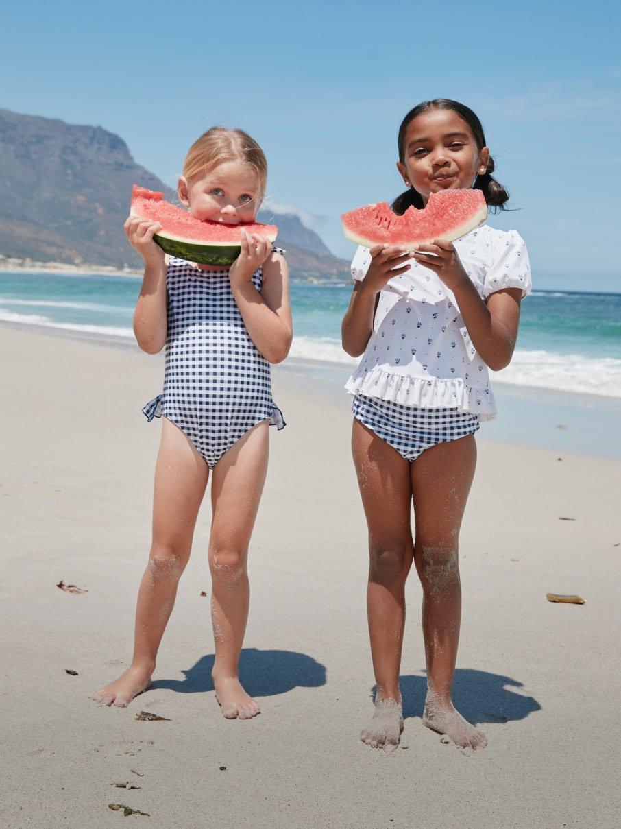 two little girls standing on a beach eating watermelon