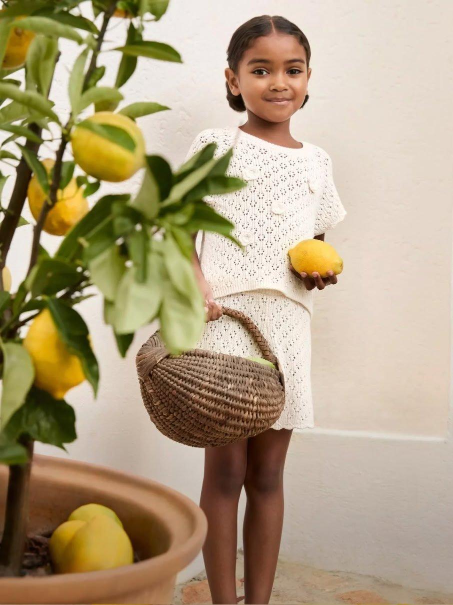 a young girl holding a basket of lemons and a potted plant